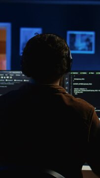 Engineer wearing headphones while using coding to fortify security, remotely working for IT company. Software expert listening music and upgrading binary code scripts on computer, camera B