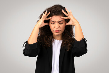 Stressed young businesswoman with pained face expression, holding her head in frustration or...