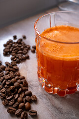 Freshly squeezed carrot juice in a crystal glass glass next to coffee beans