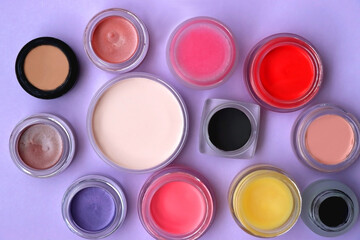 Bowls with various colorful cream beauty products on purple background. Top view.