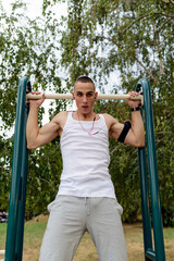 Obraz premium Man doing pull ups in the park.Young athletes train at the gym in the open.