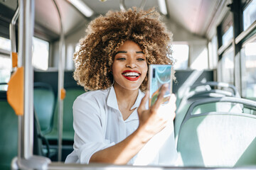  Beautiful and fashionable black woman standing in city bus. She is happy and smiled while using...