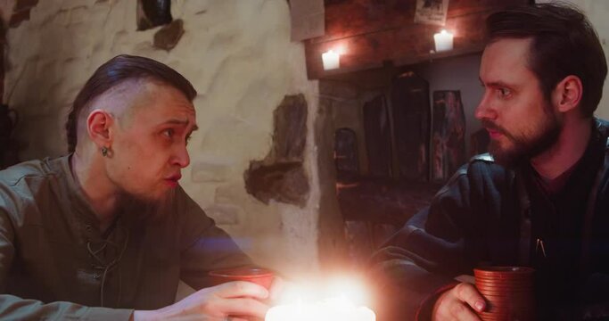 Guy talks to friend drinking in tavern. Bearded man tells interesting tale to fellow in medieval pub. Guests with alcohol beverages in old hotel