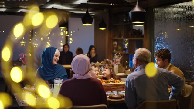 Muslim Family Sitting Around the Restaurant Table in Ramadan or on Eid. Crescent and Star Motifs. Meat and Sweets on the Table