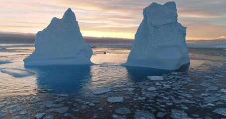 Two Antarctic melting icebergs in sunset landscape. Drone flight between glacier melted hole floating in ice ocean water. Global warming and climate change. Travel, explore Antarctica wild nature