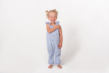 Cheerfully laughing little girl in blue overall standing looking at camera