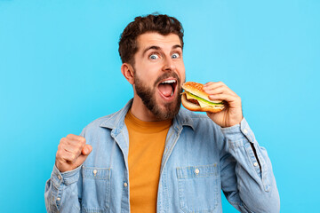 Excited Caucasian man by gesturing YES holding hamburger in studio