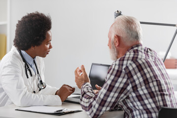 Doctor specialist consulting a patient in a doctor's office at a clinic. Female doctor is talking with a male elderly patient.