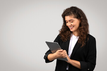 Fototapeta premium Young businesswoman in black suit using digital tablet, reviewing important documents or chatting online with clients