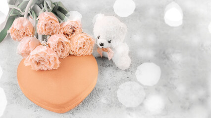 Heart shaped peach fuzz velvet gift box with tulips and a teddy bear on a gray background with...