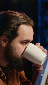 Computer scientist drinking cup of coffee while developing code on PC using java programming languages. IT admin brainstorming ways of fixing database errors, enjoying hot beverage, camera A
