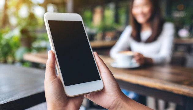 Mockup image of hand holding white mobile phone with blank black screen in vintage cafe