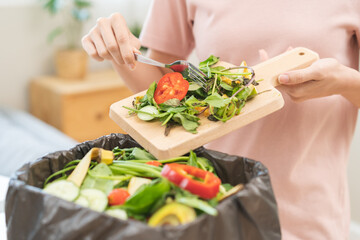 Obraz na płótnie Canvas Compost from leftover food, asian young housekeeper woman hand holding cutting board use fork scraping waste, rotten vegetable throwing away into garbage, trash or bin. Environmentally responsible.