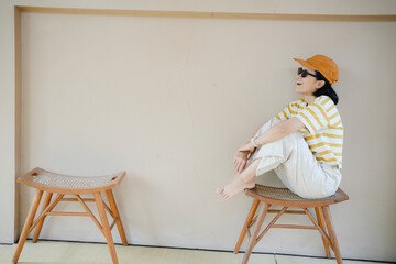 Happy Asian woman sitting on wooden chair on cream wall background.