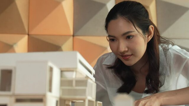Closeup of professional asian female architect engineer looking while checking at house model at office. Checking real estate house. Business design and building construction concept. Manipulator.