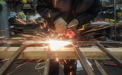 Sparks from the grinder when cleaning a metal structure. A metalworker strips metal with a grinding stone.