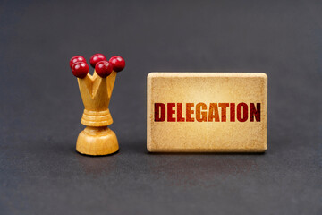 On a black surface there is a chess piece and a wooden block with the inscription - Delegation