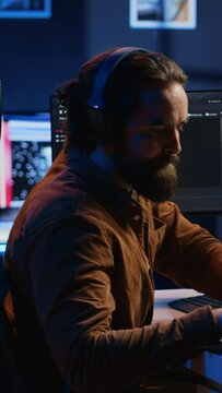 Programmer does multitasking to finish developing PC code, drinks coffee, listens music. IT admin wearing headphones, enjoying hot beverage, solving database errors on computer and laptop, camera A