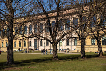 Fototapeta na wymiar Munich, Germany 02.03.2024. Many people enjoy the spring sunshine at the popular place in front of the Alte Pinakothek in Munich, Germany. Looking through some bare trees