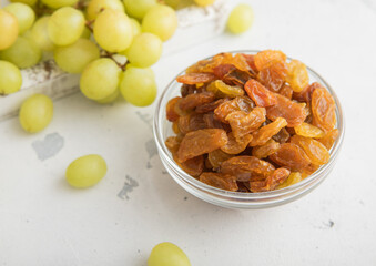 Sweet dried green raisins in glass bowl with ripe grapes in wooden box on light kitchen background.