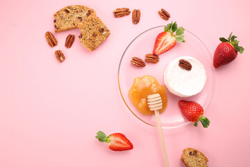 Brie cheese with strawberries, pecans nuts, crackers and honey on pink background. Flat lay. Copy space