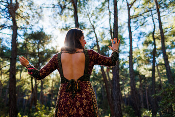 Young beautiful woman dancing in the forest with her hand raised.
