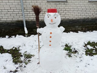 A snowman made of fresh white snow with a carrot nose and red pelvis on his head and holding a...