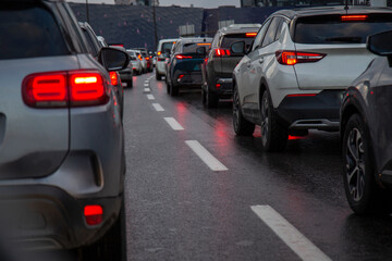 Traffic jam with a row of cars on a highway during rush hour in the evening after work. red brake lights of stopped cars on the background of wet asphalt with white lanes at sunset