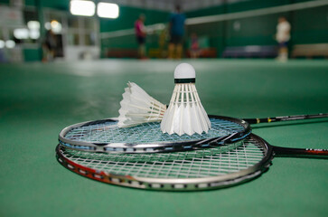 Badminton rackets and white cream badminton shuttlecocks after playing or after games on green floor in indoor badminton court  soft focus  concept for badminton lovers around the world.