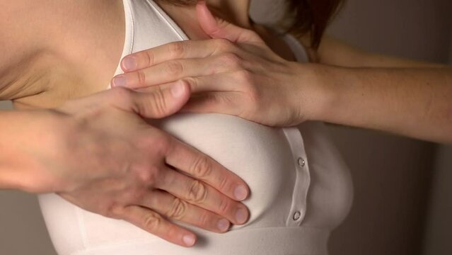 A health-conscious woman is performing a self-examination self-check for signs of breast cancer. She inspects her breast, palpating with her fingers to check for any unusual lumps or abnormalities. 