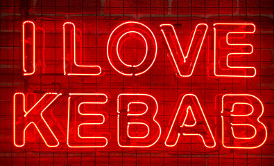 Neon shining sign in red color on a brick wall with the inscription or slogan I love kebab. Brick wall, background. Bright electric neon light. Cafe-restaurant Doner Kebab.