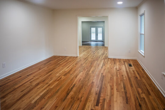 A house for sale with an empty white living room with a double wide entrance to the dining room of a newly renovated and painted house with dark hardwood floors