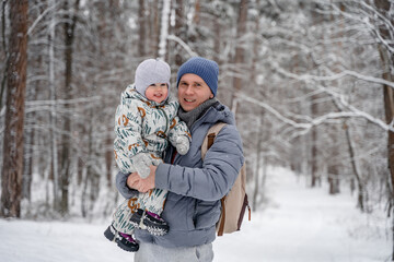 A young father and a littl child of 2 years old are laughing and having fun in a snowy winter forest on a walk