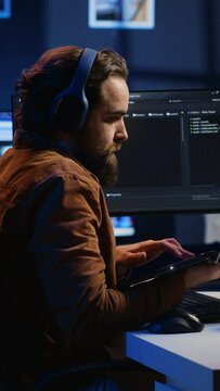 Developer focused on typing complex code in neon lit home office, listening music and developing software application. IT expert wearing headphones, solving coding project tasks on laptop, camera A
