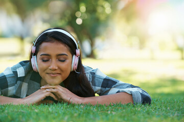 Music headphones, park or woman on grass to relax for rest in garden, nature or field with smile or peace. Eyes closed, streaming or calm person on break with playlist for radio, podcast or wellness