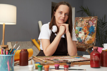 Watercolor artwork in studio. Creative education for aspiring artists. Charming kind Caucasian woman wearing brown apron painting in art creative studio
