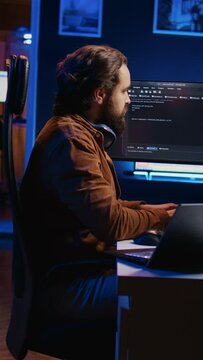 Technician typing code in neon lit personal office, using javascript programming language to develop software application. It specialist using multimonitor desktop setup to finish project, camera B
