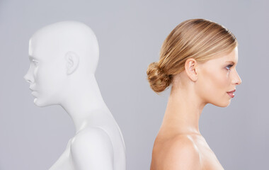 Studio, woman and profile of mannequin with beauty versus artificial standard, perfect and facial wellness. Girl, doll and clone of face for cosmetics, plastic surgery or makeup on grey background.