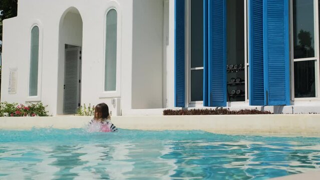 Little girl jumping into the water of a swimming pool, slow motion. Summer vacation and travel concept 