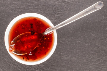 Strawberry jam in a white ceramic saucer with a metal spoon, macro, top view.