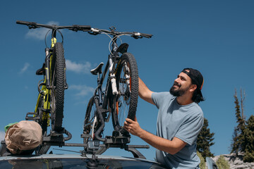 A man puts bicycles on the roof of a car on a mountain road.