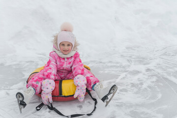 A little girl of 5 years old sits on a tubing and relaxes after skating on white figure skates at the skating rink in winter.