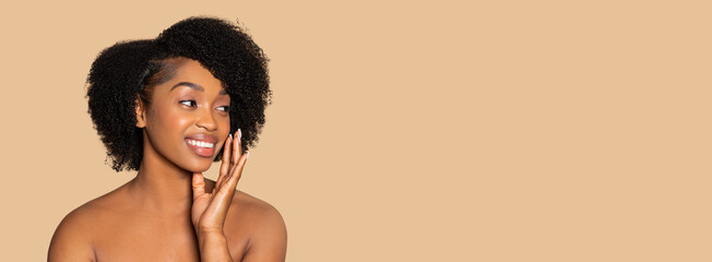 Young black woman applying cream to cheek, looking away at free space