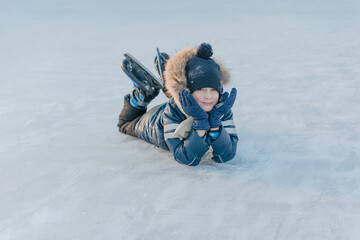 7 year old boy lying on the ice, skates on his feet, resting from skating. Winter fun.