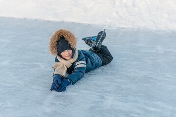 7 year old boy lying on the ice, skates on his feet, resting from skating. Winter fun.