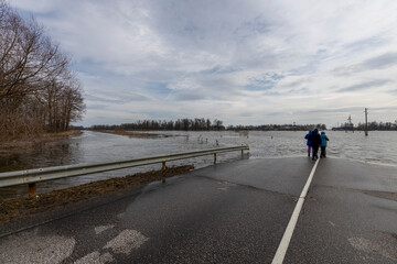 people near a flooded road, early spring flood, river overflowing its banks, environmental pollution, ecology