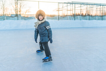 Adorable little boy in winter clothes skating on the ice rink