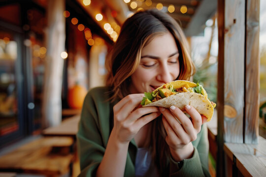 Portrait of young woman eating a delicious taco in restaurant outdoors