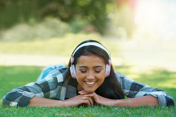 Woman, headphones and streaming song on grass, peace and calming podcast in outdoors. Female person, happy and relaxing on lawn, weekend playlist and subscription for audio or sound on vacation
