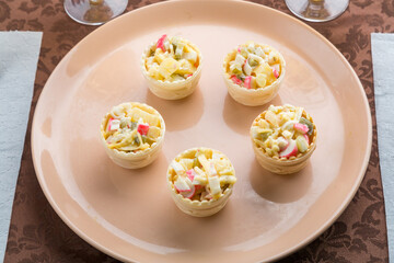 on the table is a salad in tartlets in a beige plate on a brown tablecloth